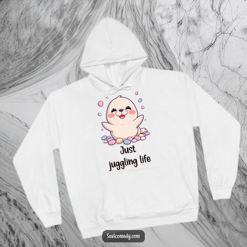 Funny seal hoodie showing a seal happily juggling shiny pebbles with a wide grin, perfect for cozy, humorous relaxation.