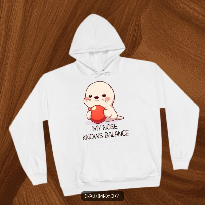 Funny seal hoodie, cute character balancing red ball on nose, playful and skillful illustration, warm and cozy apparel, perfect funny gift for animal lovers.